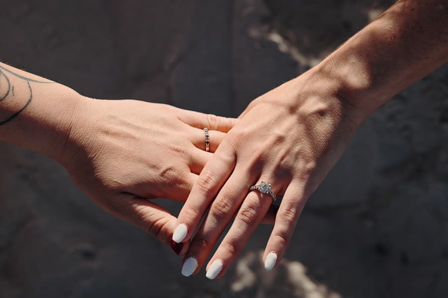 Close-up of the couple's hands showing engagement rings, with soft sunlight highlighting the details.