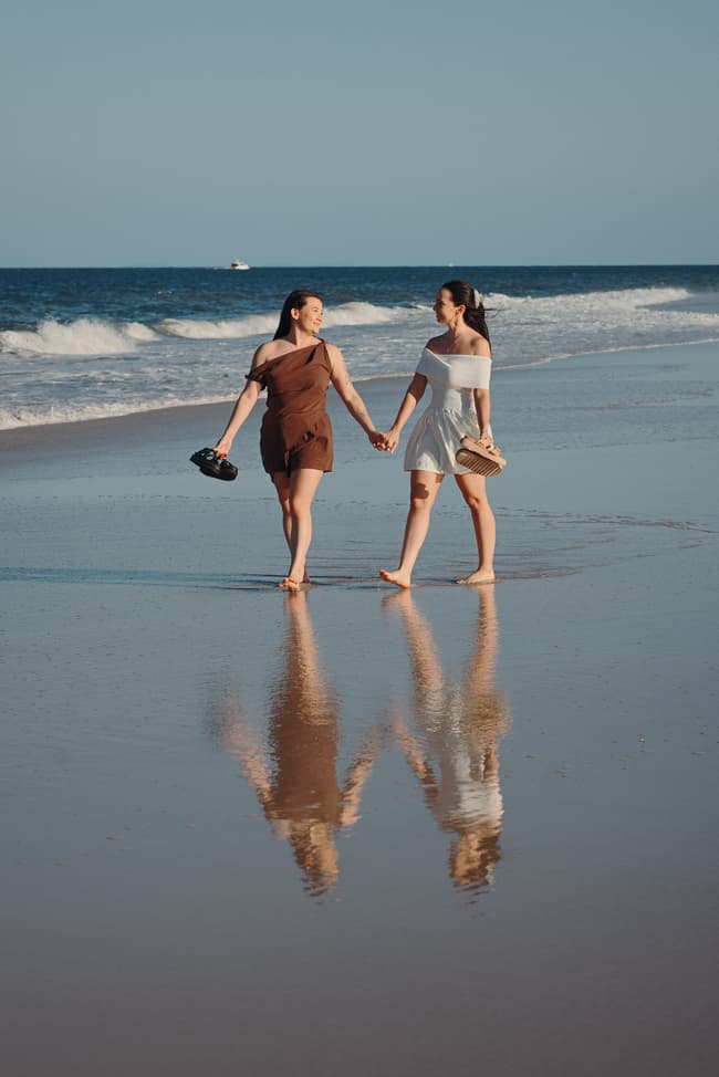 The couple walks hand in hand along the shoreline at Woorim Beach, holding their shoes, with gentle waves in the background.
