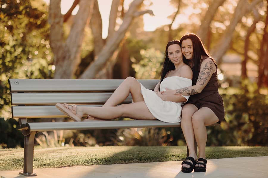The couple sits closely on a park bench, surrounded by trees, enjoying a peaceful moment together.