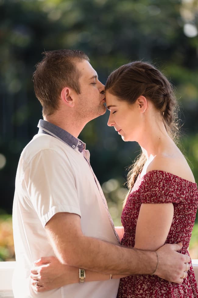 The couple embracing, one partner kissing the other's forehead, in a serene garden setting at The Abbey Cobaki.