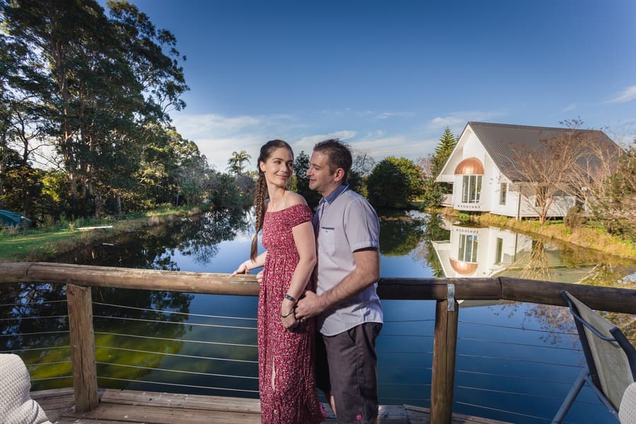 The couple standing on a deck, with a scenic lake and chapel in the background at The Abbey Cobaki.