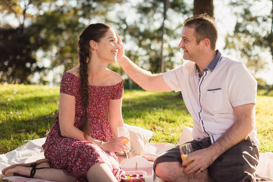 The couple enjoying a picnic, one partner gently touching the other's hair, smiling warmly at The Abbey Cobaki.