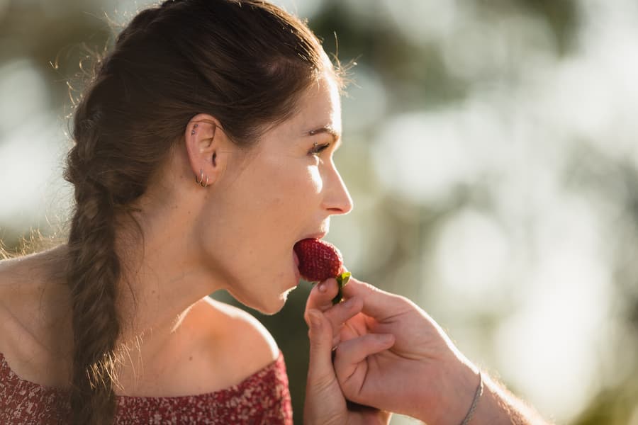 Close-up of one partner feeding a strawberry to the other, with soft natural light at The Abbey Cobaki.