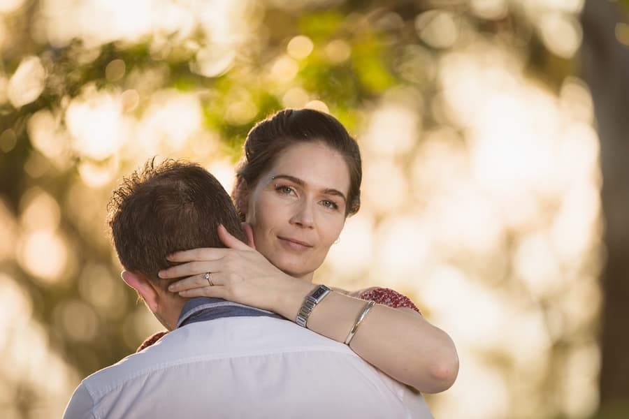 One person embraces the other, looking at the camera with a serene expression, in soft evening light.