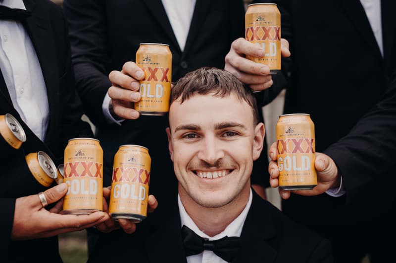 Kyle, the groom, smiles at the camera surrounded by groomsmen holding cans of XXXX Gold beer at The Tides.