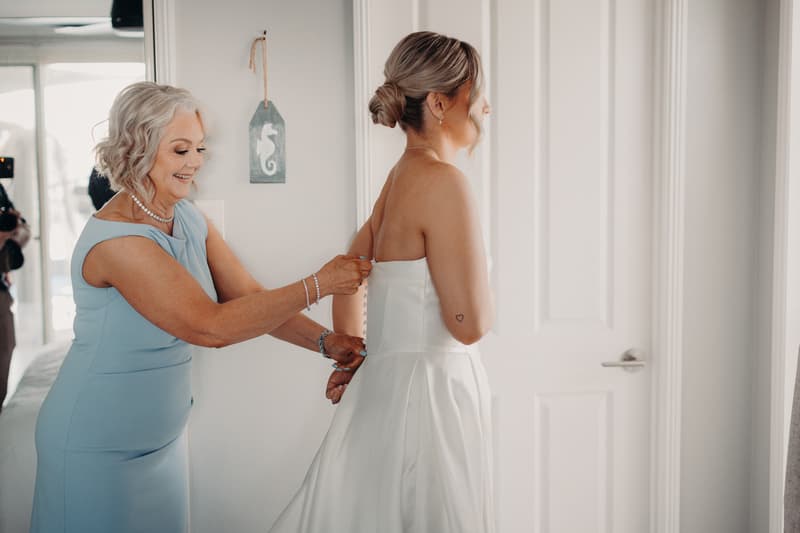 The mother of the bride helps Libby, the bride, button up her wedding dress at The Tides.
