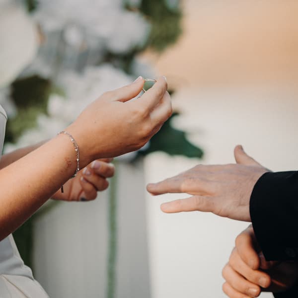 The bride holds a wedding ring near the groom's outstretched hand during the ceremony at The Tides — The Water's Edge.