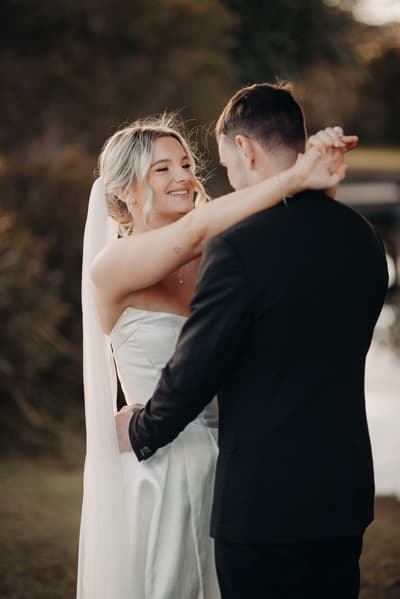 Bride Libby and groom Kyle embrace during couple portraits at The Tides, with Libby smiling and wearing a strapless wedding gown and veil, and Kyle in a black suit.