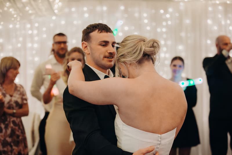 Bride Libby and groom Kyle share a dance at the reception in The Pandanus Room at The Tides, with guests watching in the background.