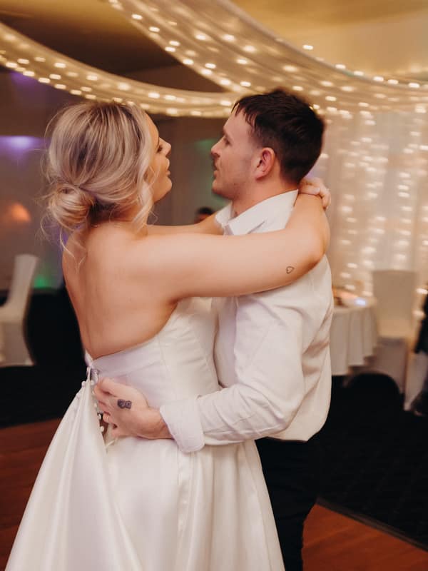 Bride Libby and groom Kyle share a dance at the reception in The Pandanus Room at The Tides, with guests seated and watching in the background under string lights.