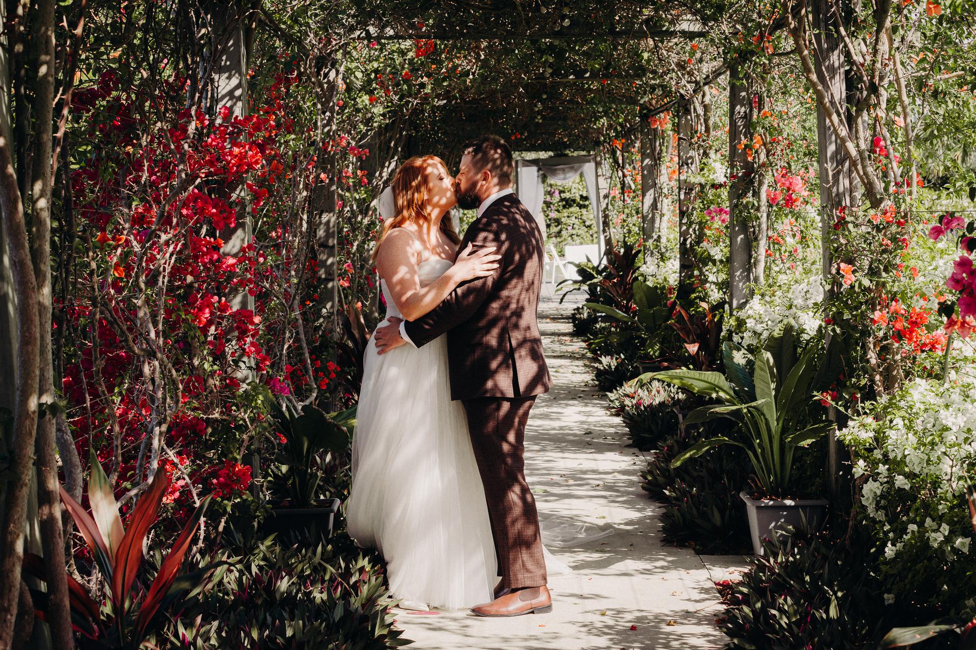 The bride Lilas and groom Kaine kiss under a floral pergola at Eatons Hill Hotel during their couple portraits session.