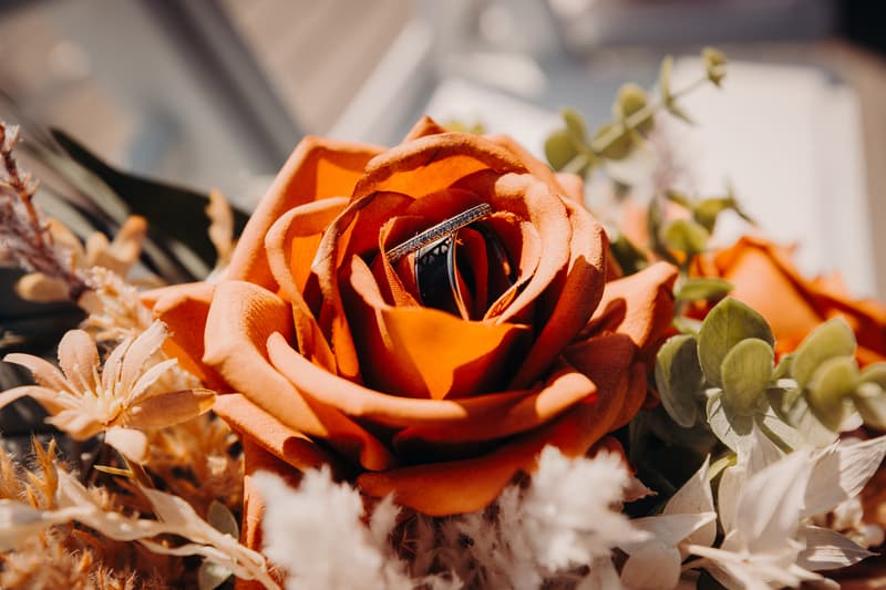 Close-up of wedding rings nestled inside an orange rose surrounded by other flowers at Eatons Hill Hotel.