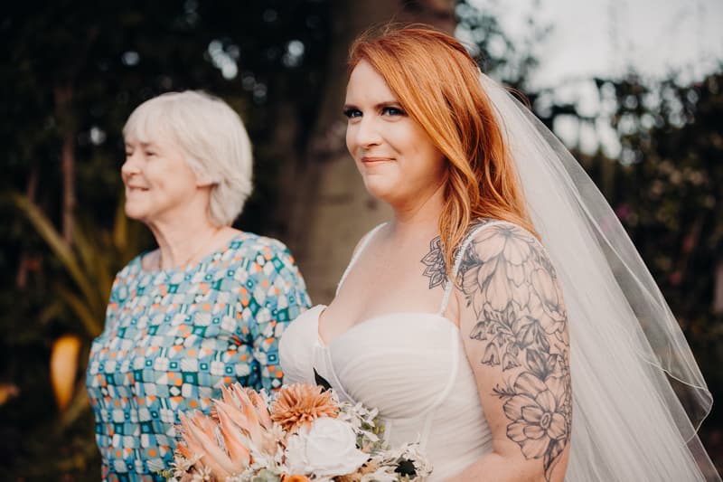 The bride Lilas stands outdoors at Eatons Hill Hotel — Lakeside holding a bouquet, accompanied by an older woman who is likely the mother of the bride.