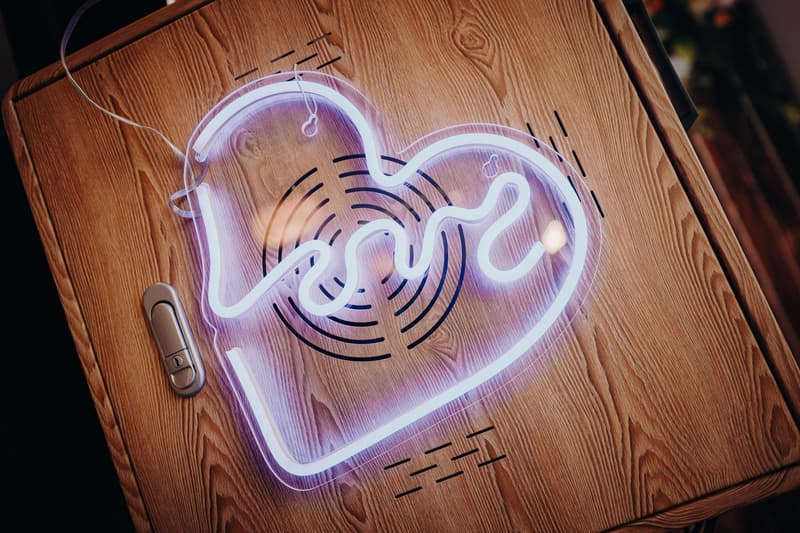 A neon light shaped like a heart with a wavy line inside is placed on a wooden surface with a metal latch on the left side.
