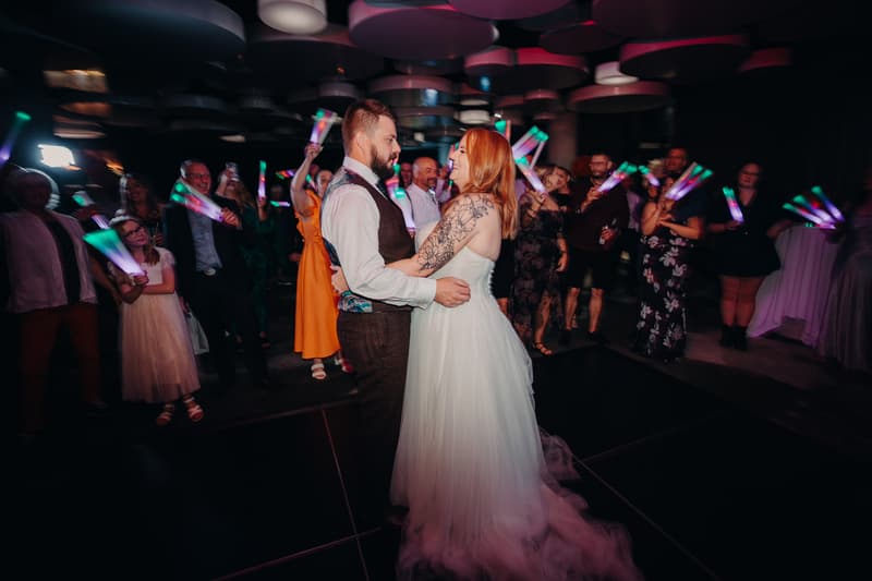Bride Lilas and groom Kaine share a dance on the dance floor at Eatons Hill Hotel — Hills Room, surrounded by guests holding glowing light sticks.