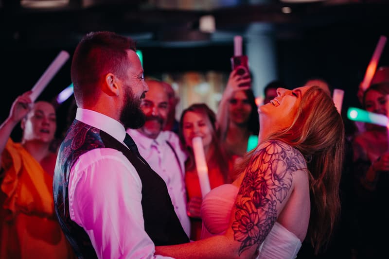 Bride Lilas and groom Kaine share a joyful moment on the dance floor at the Eatons Hill Hotel — Hills Room, surrounded by guests holding light sticks and capturing the moment on phones.
