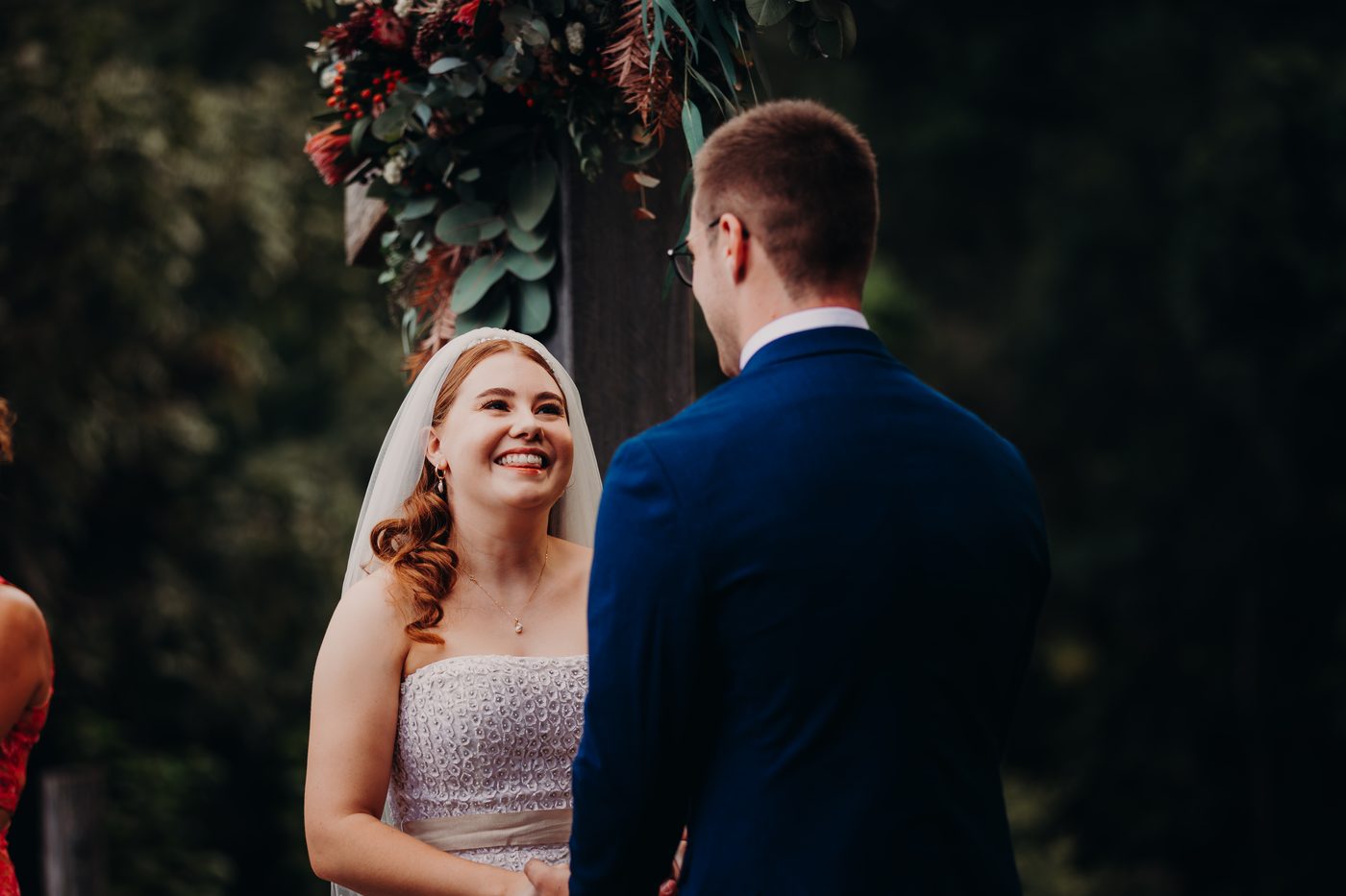 Bride Lilly and groom Connor stand facing each other under a floral arch. Basic ceremony video by She Said Yes.