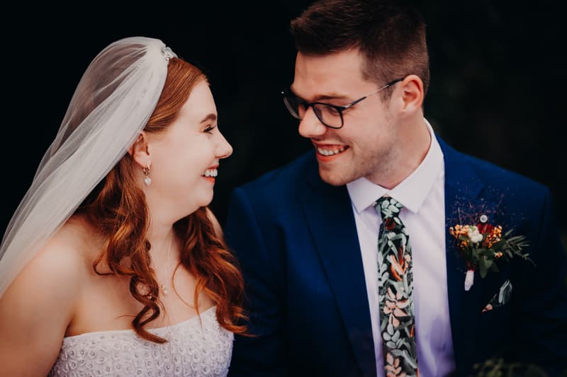 Bride Lilly and groom Connor smile at each other during their wedding ceremony at Yabbaloumba Retreat — By The River.