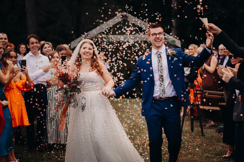 Bride Lilly and groom Connor walk down the aisle at Yabbaloumba Retreat — By The River while guests throw confetti.
