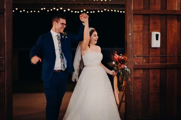 Bride Lilly and groom Connor enter the reception stage at Yabbaloumba Retreat — The Shed, holding hands with Lilly carrying a bouquet.