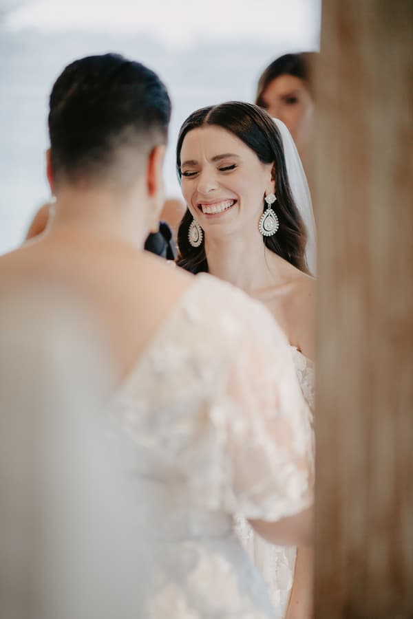 Bride smiling with eyes closed facing the groom during a wedding moment indoors.