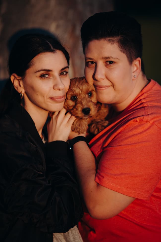 The couple holding a small dog together, smiling softly at the camera.