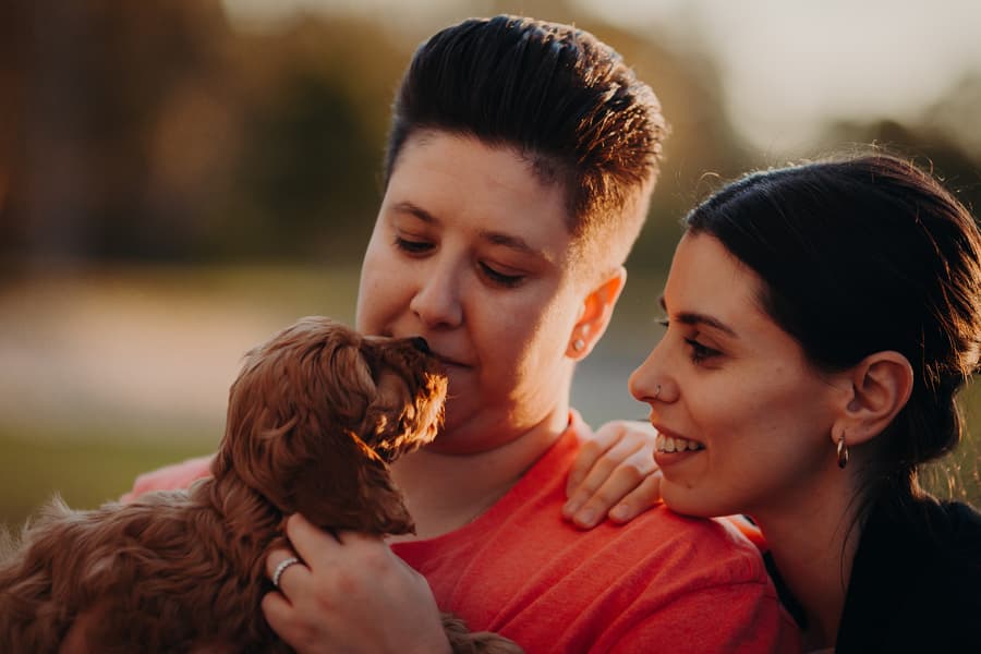 One person holding a small dog close, while the other looks on lovingly.