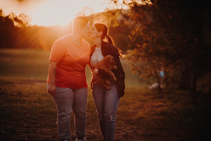 The couple shares a kiss at sunset, holding a dog, with a warm glow illuminating the scene at Hillstone St Lucia.