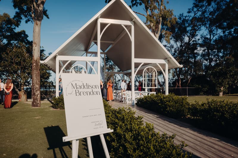 Wedding ceremony setup at Sandstone Point Hotel — Pavilion with a welcome sign for Madison and Brendon and guests gathering near the altar.