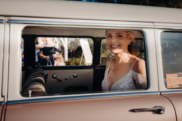 The bride Madison sits inside a vintage car smiling, visible through the open window. Wedding photography contracts by She Said Yes.