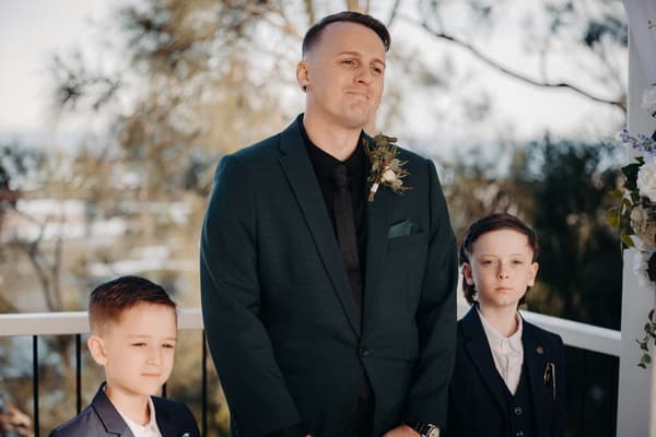 The groom stands with two young boys, all dressed in suits, at the. Brisbane videographer by She Said Yes.