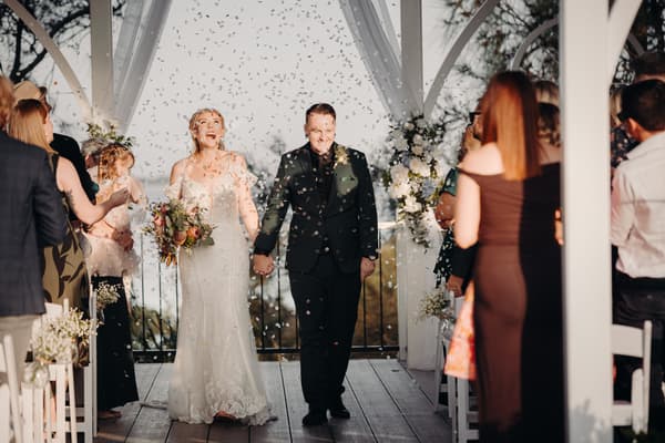 Bride Madison and groom Brendon walk down the aisle holding hands at Sandstone Point Hotel — Pavilion as guests throw confetti.