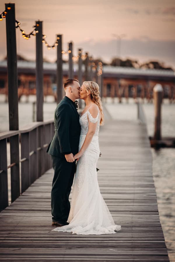 Madison and Brendon share a kiss while holding hands on a wooden pier at Sandstone Point Hotel during their couple portraits session.