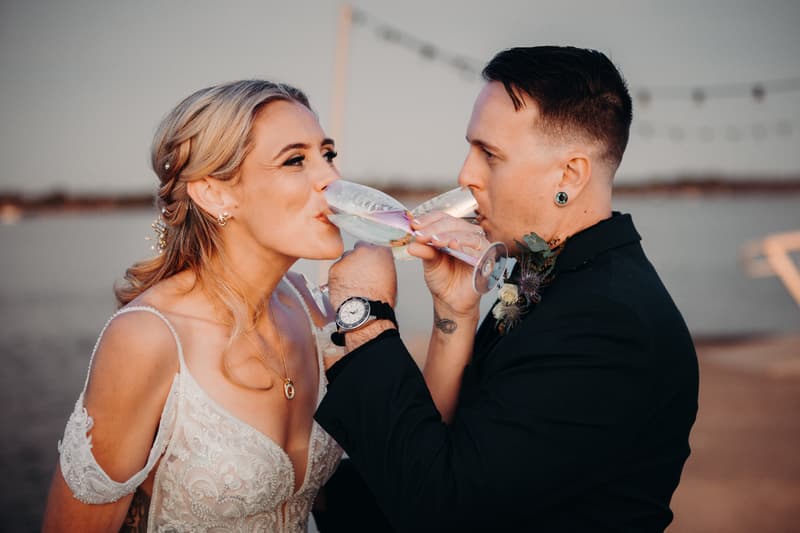 Madison and Brendon drink champagne from intertwined glasses during their couple portraits session at Sandstone Point Hotel.