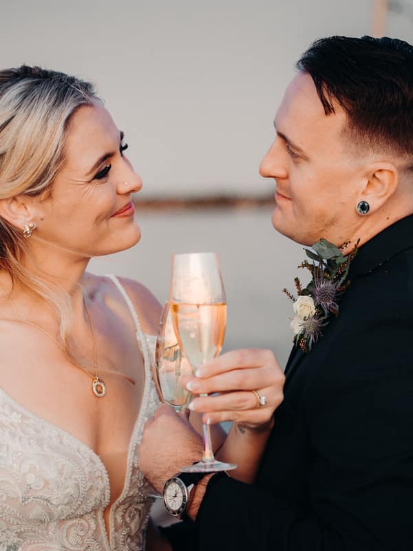 Madison the bride and Brendon the groom toast with champagne flutes at Sandstone Point Hotel during their couple portraits session.