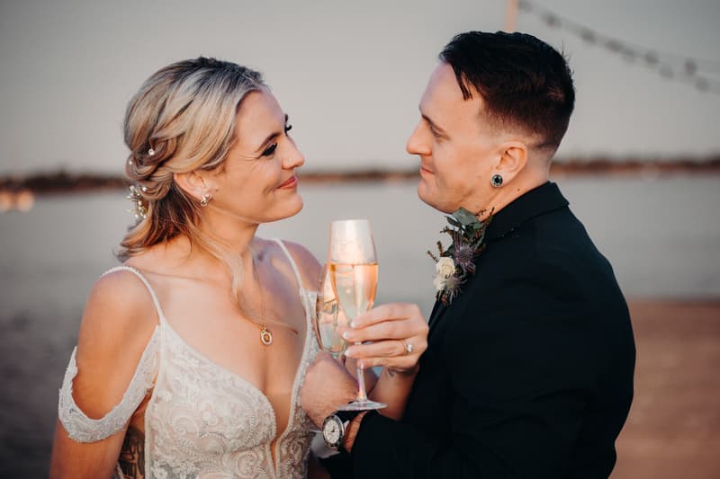 Madison the bride and Brendon the groom toast with champagne flutes at Sandstone Point Hotel during their couple portraits session.