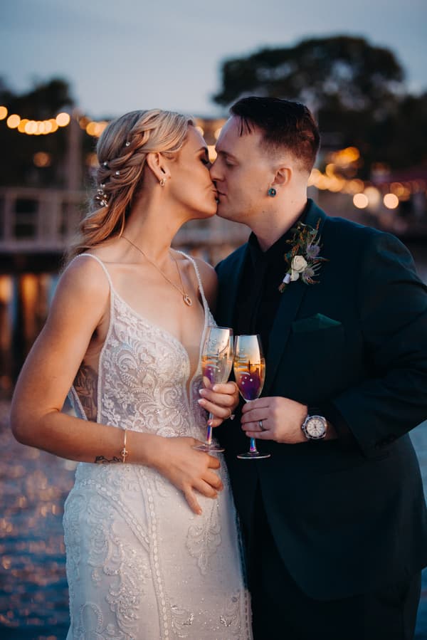 Madison and Brendon share a kiss while holding champagne glasses during their couple portraits at Sandstone Point Hotel.