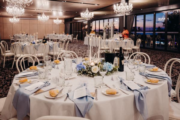 Reception tables set with white tablecloths, blue napkins, bread rolls, glassware, and floral centerpieces with candles in the Pumicestone Room. ABIA Awards wedding photography by She Said Yes.