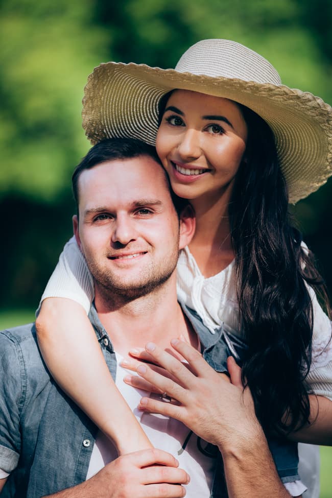 The couple poses closely, with one embracing the other from behind, both smiling warmly.