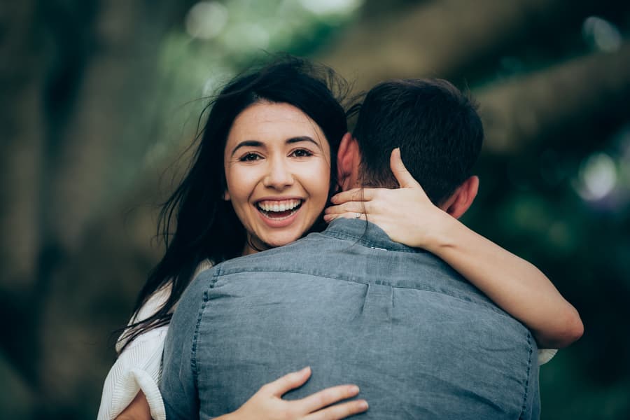 Close-up of the couple embracing, with one smiling brightly, against a blurred natural background.