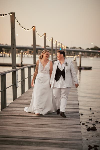 Brides Mandy and Selina walk hand in hand on a wooden pier. Ekka week Brisbane wedding by She Said Yes.