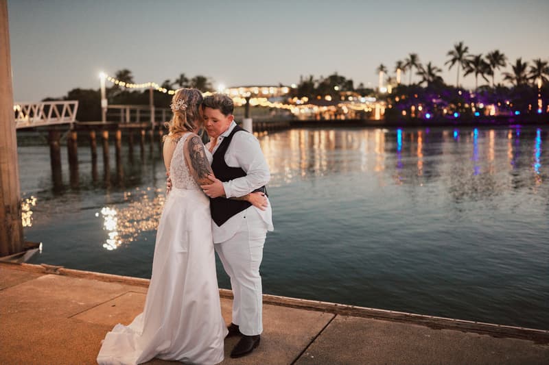 Brides Mandy and Selina embrace near the water at Sandstone Point Hotel during their couple portraits session at dusk.