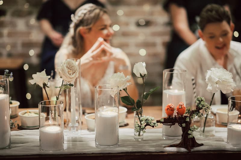 Mandy and Selina sit at a decorated table with white flowers and candles at Sandstone Point Hotel — The Cellar during the reception stage.