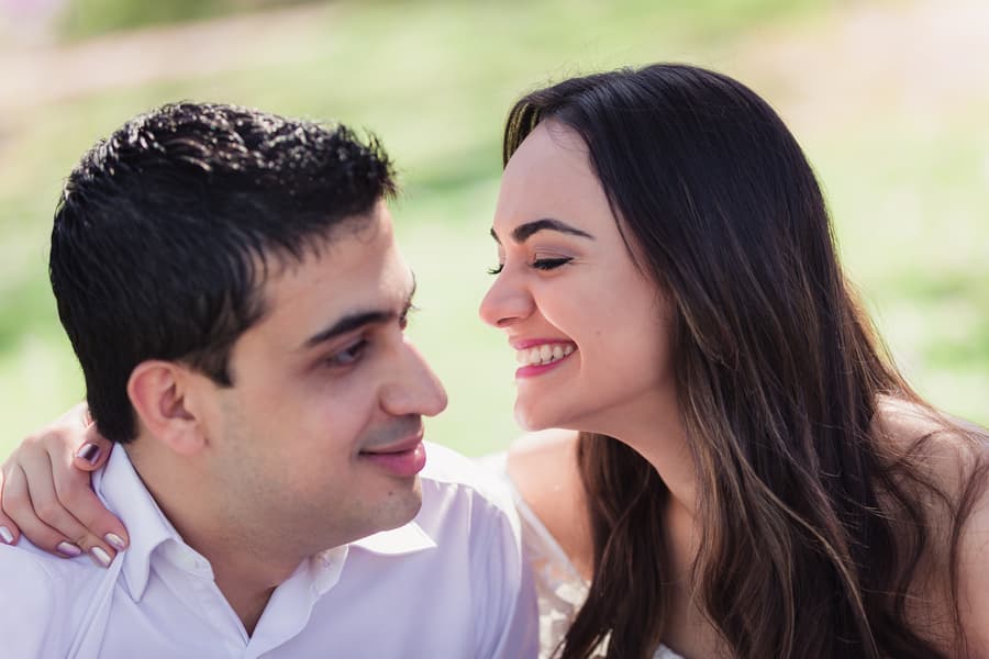 Close-up of the couple smiling at each other, sitting on a picnic blanket at UQ Lakes.