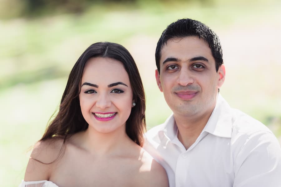 The couple smiles warmly at the camera, sitting together on a picnic blanket at UQ Lakes.