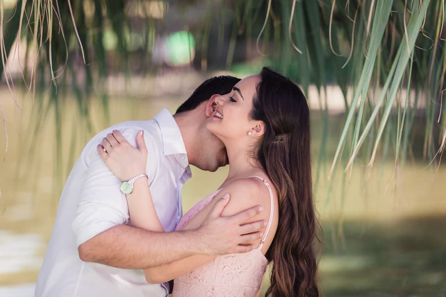 The couple embraces under lush greenery at UQ Lakes, with soft light filtering through leaves.