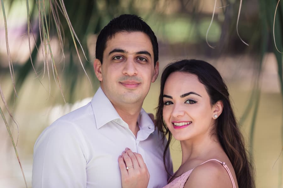 The couple stands close together, smiling at the camera, with greenery in the background at UQ Lakes.