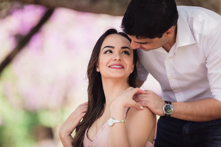 The couple shares a tender moment, with one looking lovingly at the other, surrounded by purple blooms.