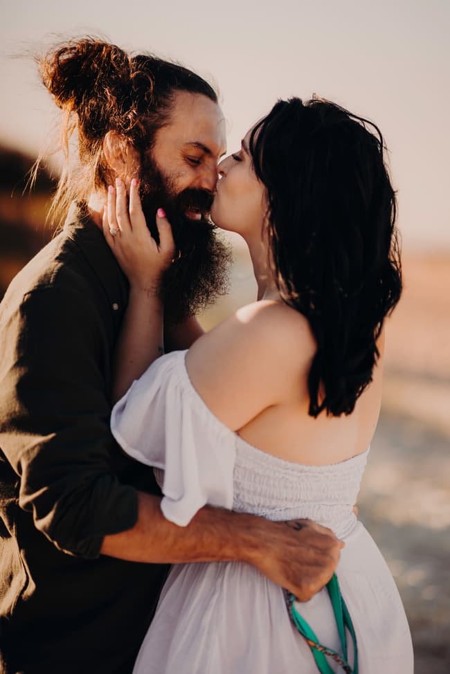 The couple shares a kiss on the sand at Woorim Beach, surrounded by soft, golden light. Their embrace is tender and affectionate.