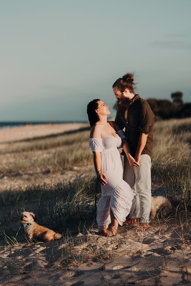 The couple stands holding hands on the grassy dunes at Woorim Beach. They gaze into each other's eyes, surrounded by the calm beach landscape.